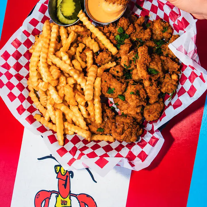 Basket of Lulu's Gator Bites served with crinkle-cut fries, pickles and dipping sauces.